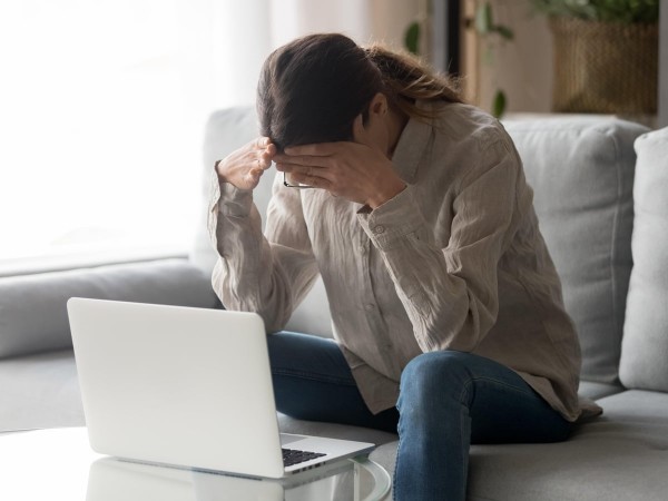 woman with her head in her hands, sitting in front of laptop
